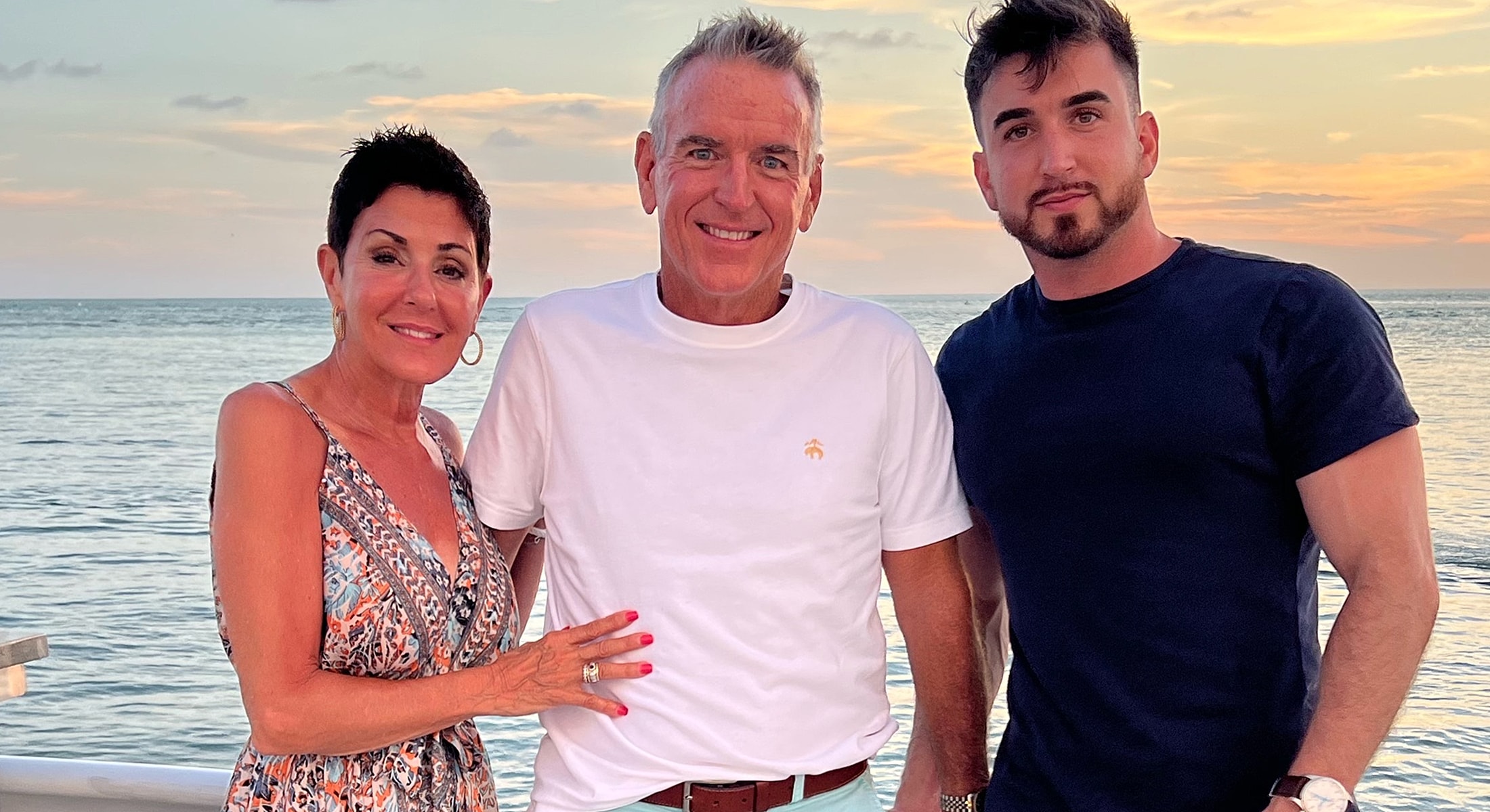 Three people posing by the ocean at sunset.